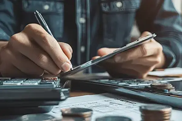 This image depicts a person working with financial documents, calculating or analyzing finances, with a calculator and coins on the table.